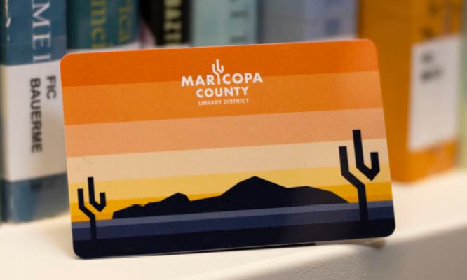 A Maricopa County Library District library card sitting on a bookshelf